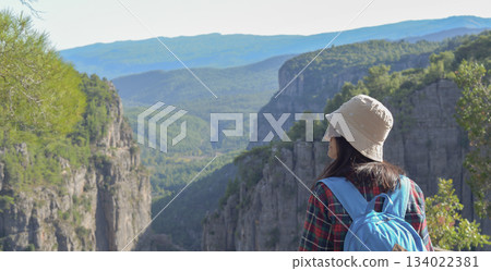 Rear view, a woman traveling through the mountains of Turkey with a backpack on the edge of the Tazi Canyon admiring the mountains, a girl outdoors enjoying the view of the Tazi Canyon. 134022381