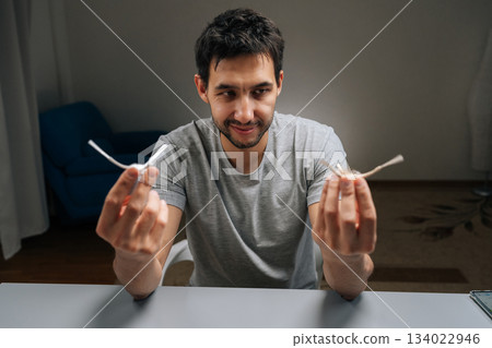 Portrait of male holding in hand and examining tangled dirty side brush from robot vacuum, illustrating maintenance, replacement and improved smart home cleaning efficiency and hygiene. 134022946