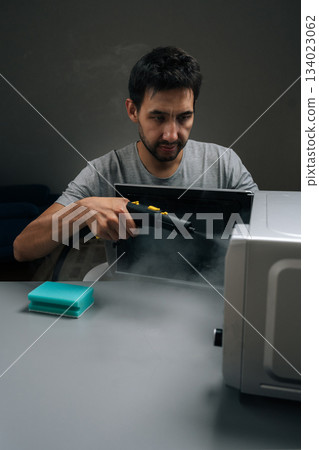 Vertical portrait of professional housekeeper cleaning and sanitizing microwave oven with steam cleaner device, eliminating germs and tough stains, maintaining hygiene in kitchen at home. 134023062