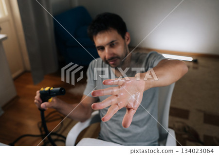 Man finding humor in everyday household chores, fooling around with steam cleaner holding out his wet, sweaty hand in playful gesture, adding lightheartedness to cleaning routine. 134023064