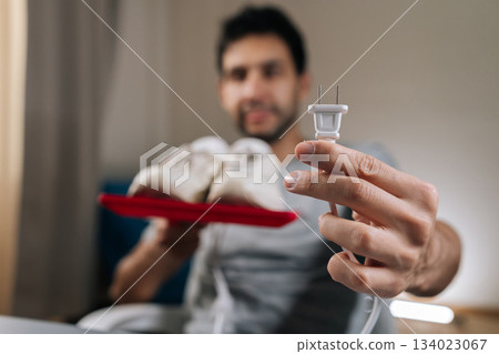 Focus on foreground of blurred male holding electric plug for shoe dryer, preparing to clean and dry white sneakers, focusing on home care routine and footwear maintenance. 134023067