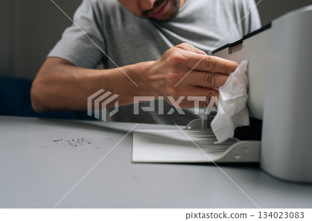 Close-up cropped shot of repairman cleaning laser printer with white wipe, focusing on maintenance and hygiene of office technology while performing service to electronic equipment. Close-up cropped shot of repairman cleaning laser printer with white wipe, focusing on maintenance and hygiene of office technology while performing service to electronic equipment. 134023083