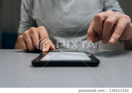 Close-up hands of unrecognizable man removing clear screen protector from onto portable e-reader device, ensuring electronic book display is protected from scratches and everyday wear. Close-up hands of unrecognizable man removing clear screen protector from onto portable e-reader device, ensuring electronic book display is protected from scratches and everyday wear. 134023102
