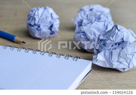 Crumpled paper balls on a wooden table, representing the repetitive cycle of creating and revising. Work in progress concept. Crumpled paper balls on a wooden table, representing the repetitive cycle of creating and revising. Work in progress concept. 134024128