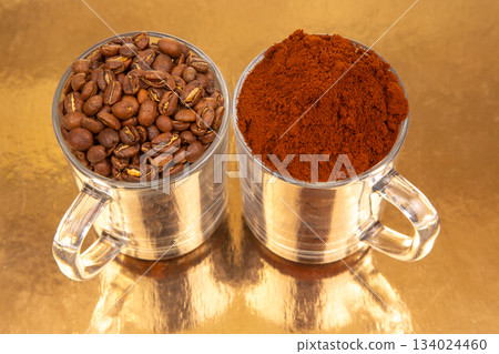 Close-up of two glass mugs on a golden background , one packed with whole roasted coffee beans Close-up of two glass mugs on a golden background , one packed with whole roasted coffee beans 134024460
