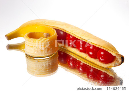Surreal food composition of a peeled banana filled with glossy cherry tomatoes 134024465