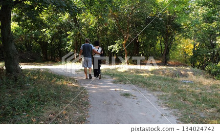 Happy couple walking along path at summer forest. Romantic pair going along trail at wild woodland. Lovers spending time together at nature. Concept of love and happiness. Slow motion Happy couple walking along path at summer forest. Romantic pair going along trail at wild woodland. Lovers spending time together at nature. Concept of love and happiness. Slow motion 134024742