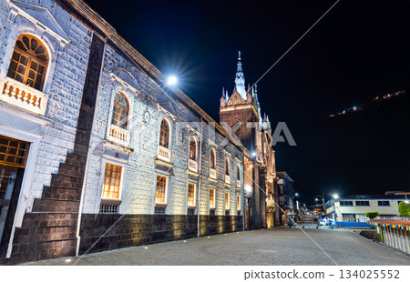 Illuminated Basilica of Our Lady of the Holy Water stands in Banos de Agua Santa, Ecuador. Semi-Gothic church features volcanic stone architecture and streetlights under night sky 134025552