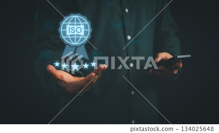 Businessman holding digital ISO certification icon with five-star rating, symbolizing international standard, quality assurance, compliance, trust, and business excellence in professional management. 134025648