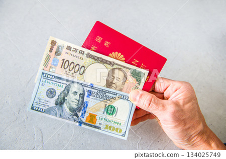 An angle shot of a person holding one US $100 bill, one $20 bill and a Japanese passport from the right front with their right hand 134025749