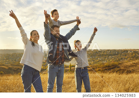 Happy family in the field looking into the distance with hands up enjoying nature together. Happy family in the field looking into the distance with hands up enjoying nature together. 134025983