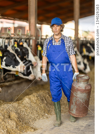 Middle-aged male farmer carrying metal milk tank Middle-aged male farmer carrying metal milk tank 134026163