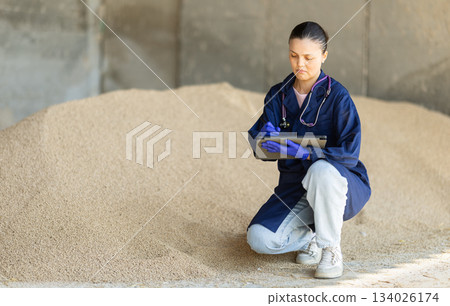 Asian woman farmer with tablet inspect granulated feed in storage Asian woman farmer with tablet inspect granulated feed in storage 134026174