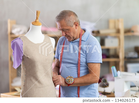 Male tailor standing in workshop checking dress 134026175