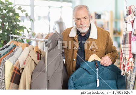 Mature male shopper chooses and tries fashionable down jacket in clothing store Mature male shopper chooses and tries fashionable down jacket in clothing store 134026204