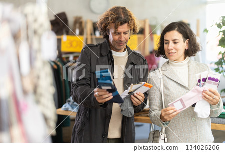 Positive couple shoppers examining and buying new warm socks in clothing store 134026206