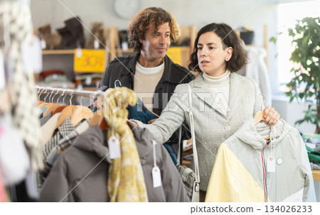 woman chooses jackets and coats next to a man who advises woman chooses jackets and coats next to a man who advises 134026233