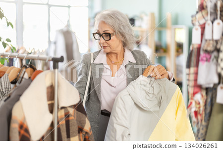 elderly woman chooses a down jacket in store 134026261