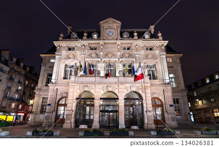 Town Hall of the 18th arrondissement in Paris, France. The historic building with a clock tower and flags stands on Place Jules Joffrin at night 134026381