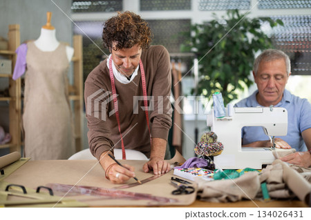 Mature man sewing clothes with assistant drawing on paper 134026431