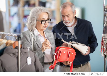 Mature couple spend time in shop and choose handbag Mature couple spend time in shop and choose handbag 134026435