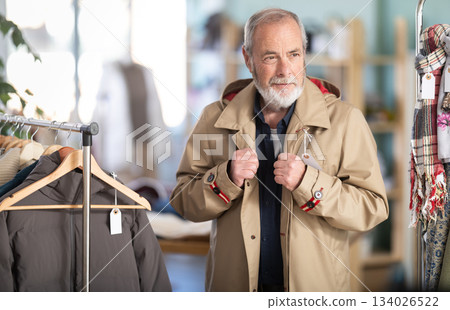 Elderly man chooses tries fashionable coat in clothing store 134026522