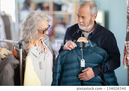 Family clothing store, senior couple customer chooses down jacket Family clothing store, senior couple customer chooses down jacket 134026540