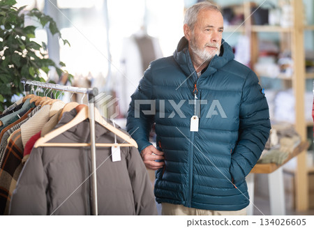 Mature male customer is trying on down jacket during shopping in store Mature male customer is trying on down jacket during shopping in store 134026605