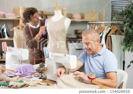 Elderly man sews on machine male assistant sews on mannequin 134026650