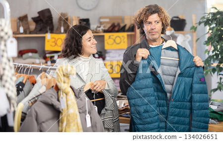 Happy european couple examine and choose new coat or down jacket for cold season in modern store 134026651