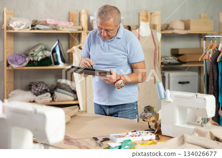 Mature man drawing on tablet in sewing salon Mature man drawing on tablet in sewing salon 134026677