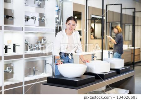 in plumbing department,thoughtful woman inspects round white ceramic sinks with faucets in plumbing department,thoughtful woman inspects round white ceramic sinks with faucets 134026695