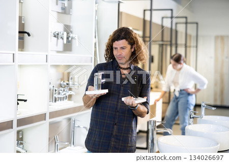 Male buyer compares black and gray stainless steel water faucets Male buyer compares black and gray stainless steel water faucets 134026697