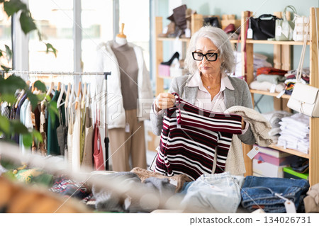 Elderly woman choosing a sweater in a store Elderly woman choosing a sweater in a store 134026731