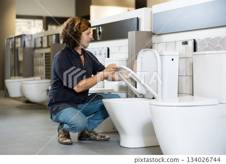 in plumbing department, male buyer checks for defects of toilet before purchasing toilet pan in plumbing department, male buyer checks for defects of toilet before purchasing toilet pan 134026744