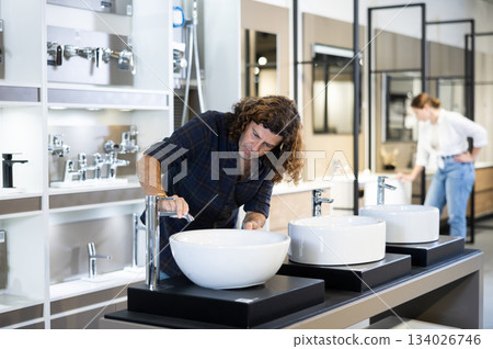 in plumbing department,thoughtful man inspects round white ceramic sinks with faucets in plumbing department,thoughtful man inspects round white ceramic sinks with faucets 134026746