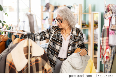 Family clothing store, senior woman customer chooses jacket or coat 134026768