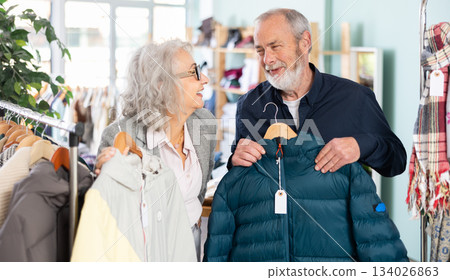 Mature married couple chooses fashionable down jacket or coat in clothing store Mature married couple chooses fashionable down jacket or coat in clothing store 134026863