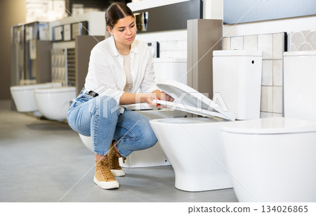 in plumbing department, female buyer checks for defects of toilet before purchasing toilet pan 134026865