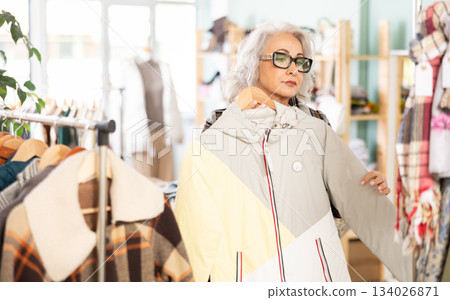 Mature woman chooses fashionable coat or jacket in clothing store 134026871