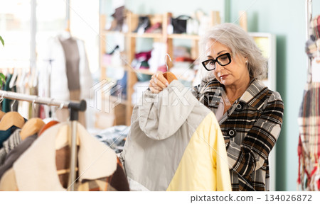 Mature woman chooses fashionable coat or jacket in clothing store 134026872