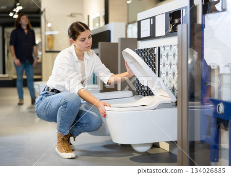 in plumbing department, female buyer checks for defects of toilet before purchasing toilet pan 134026885