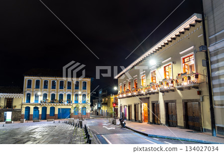 Colonial architecture lines San Francisco Square in historic center of Quito, Ecuador. White building features balconies with flower pots illuminated by streetlights under night sky Colonial architecture lines San Francisco Square in historic center of Quito, Ecuador. White building features balconies with flower pots illuminated by streetlights under night sky 134027034