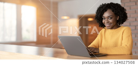 Portrait of cheerful young afro businesswoman using laptop at cafe, drinking coffee or tea, free space 134027508