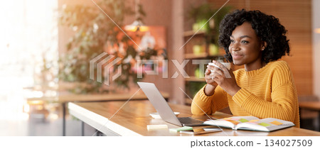 Dreamy african girl dinking tea at cafe while looking for job online, using laptop and taking notes, copy space 134027509