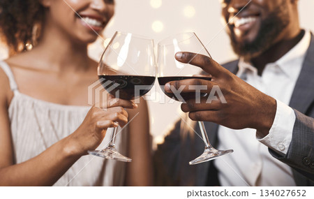 Close up of cheerful african american couple toasting with red wine, celebrating anniversary Close up of cheerful african american couple toasting with red wine, celebrating anniversary 134027652