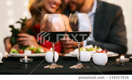 Romantic Date Background. Couple enjoying romantic dinner in restaurant, selective focus on two red wine glasses on table, panorama 134027656