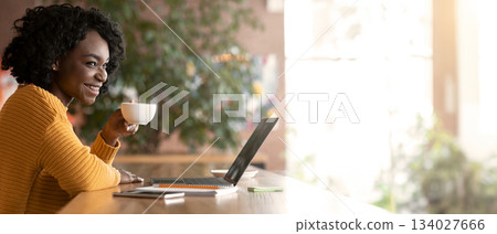 Happy african girl drinking tea while working with laptop at cafe, empty space Happy african girl drinking tea while working with laptop at cafe, empty space 134027666