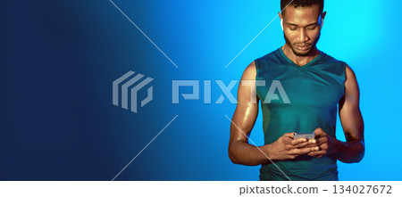 Fitness Application. Sporty Guy Using Smartphone Wearing Earphones Before Workout Standing On Blue Studio Background. Panorama Fitness Application. Sporty Guy Using Smartphone Wearing Earphones Before Workout Standing On Blue Studio Background. Panorama 134027672