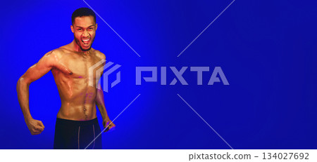 Aggressive Shirtless Black Fighter Guy Shouting Clenching Fists Ready To Fight Posing On Blue Background. Studio Shot Aggressive Shirtless Black Fighter Guy Shouting Clenching Fists Ready To Fight Posing On Blue Background. Studio Shot 134027692